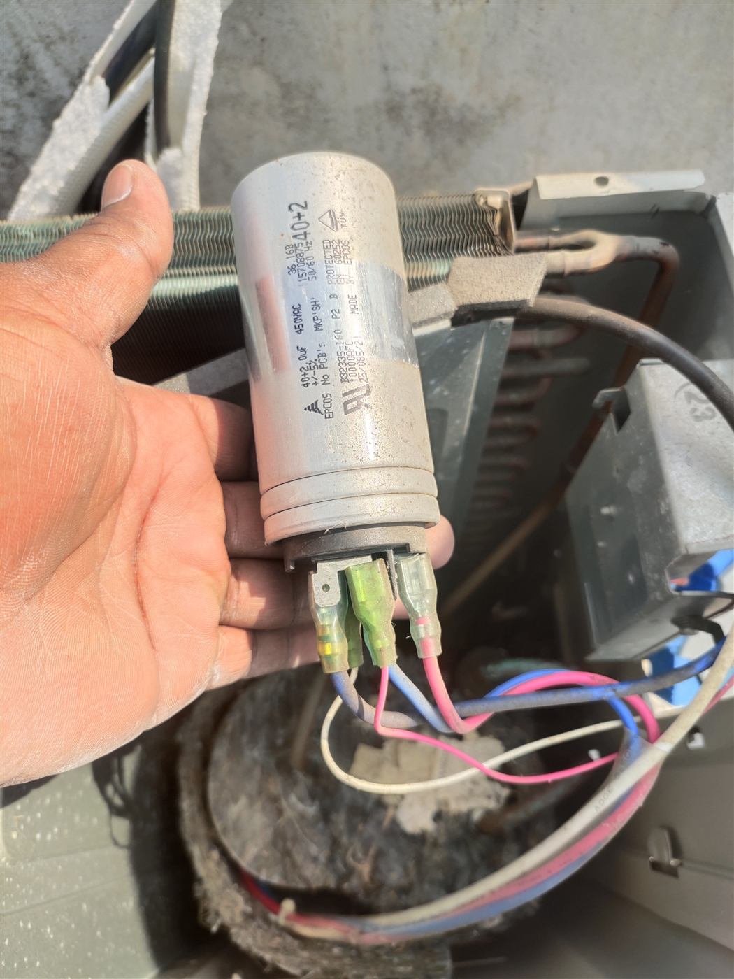 AN Repair Services technician holding a replacement AC run capacitor during a service call in Kamareddy