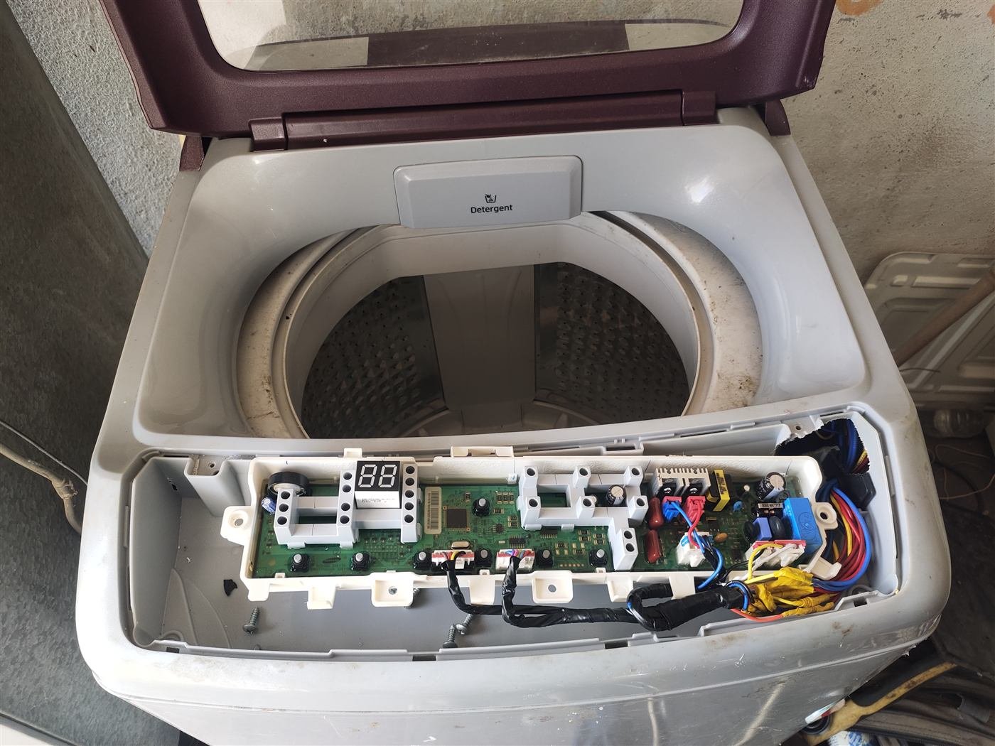 Washing machine control board and internal components exposed during a repair in Kamareddy